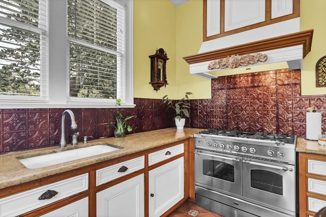 kitchen featuring range with two ovens, light stone countertops, under cabinet range hood, white cabinetry, and a sink