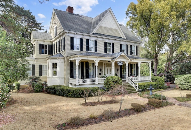 view of front of house featuring covered porch, metal roof, a chimney, and a standing seam roof