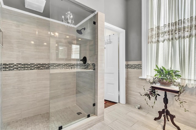 bathroom with a stall shower, tile walls, and an inviting chandelier