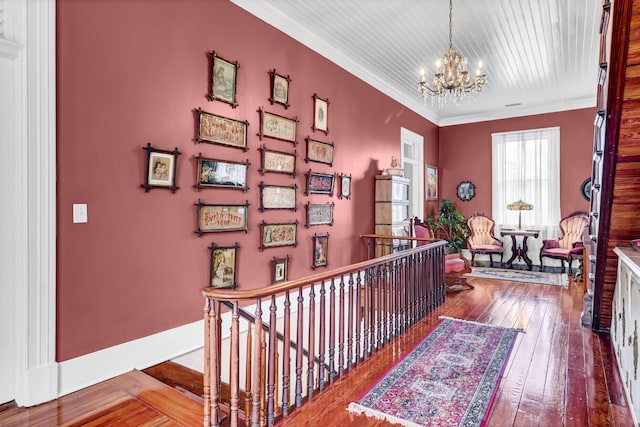 hallway featuring crown molding, wood-type flooring, an inviting chandelier, an upstairs landing, and baseboards