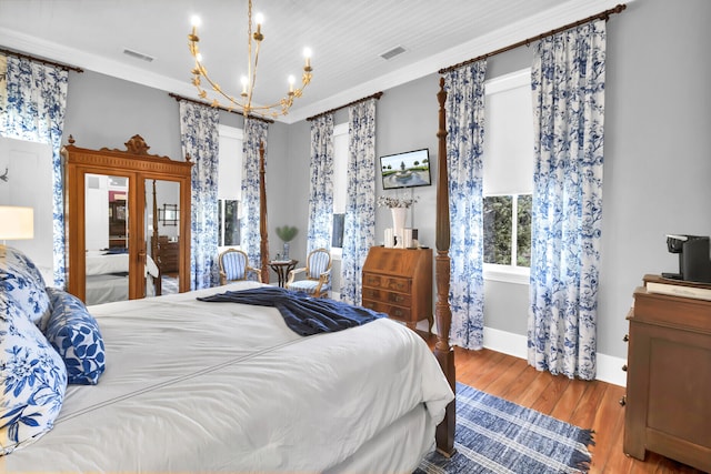 bedroom with a notable chandelier, wood finished floors, visible vents, baseboards, and ornamental molding