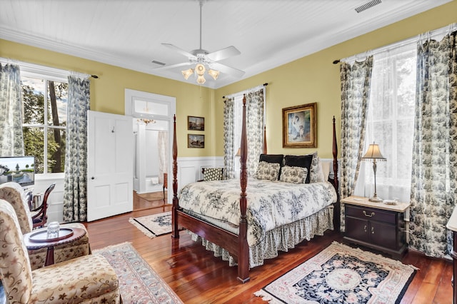 bedroom with dark wood-style floors, a wainscoted wall, visible vents, and a ceiling fan