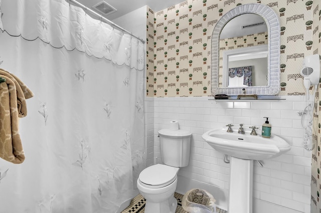 bathroom with a wainscoted wall, tile walls, visible vents, toilet, and wallpapered walls