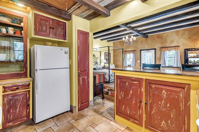 kitchen featuring freestanding refrigerator, beam ceiling, a notable chandelier, and dark countertops