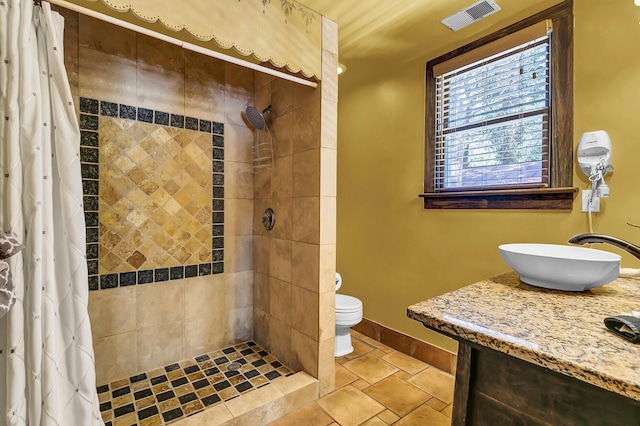 bathroom with baseboards, visible vents, toilet, a tile shower, and a sink