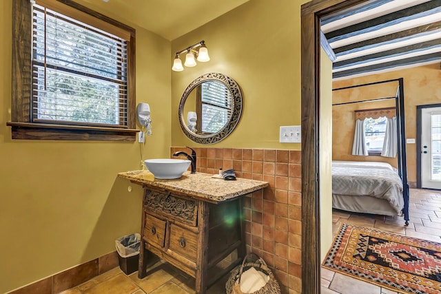 ensuite bathroom featuring a sink, tile walls, baseboards, and ensuite bathroom