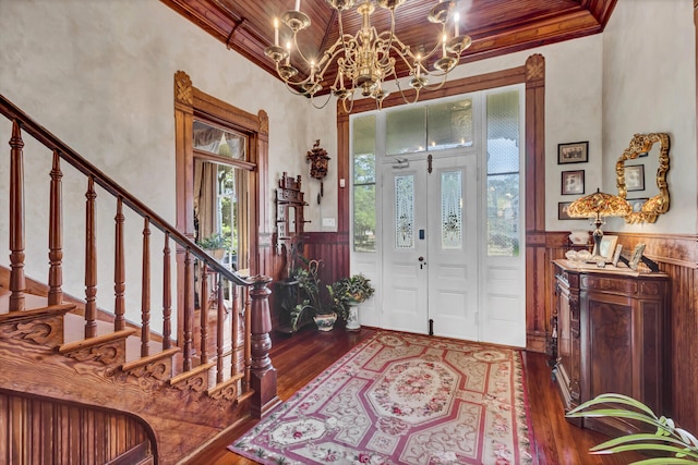 foyer with dark wood-type flooring, a chandelier, wainscoting, and stairway