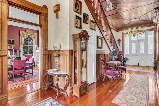 foyer entrance with wood ceiling, stairs, a chandelier, and wainscoting