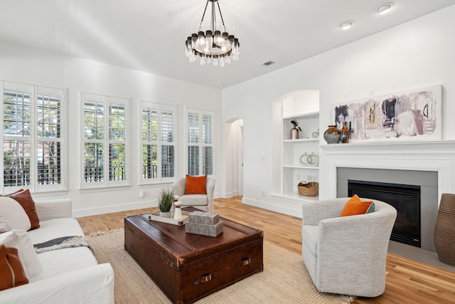 living room with a notable chandelier, built in features, and light hardwood / wood-style floors