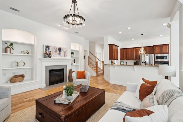 living room featuring built in features, light hardwood / wood-style floors, and a chandelier