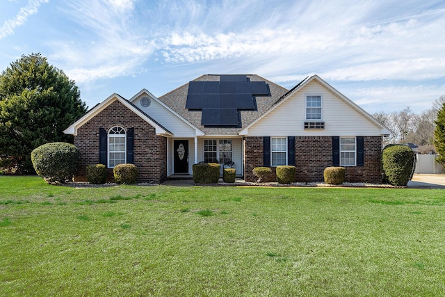 view of front of property featuring a shingled roof, a front yard, solar panels, and brick siding