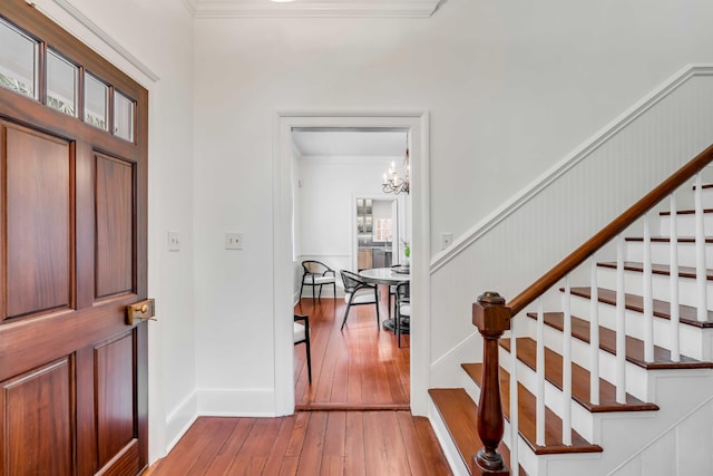 entrance foyer with light wood-type flooring, stairs, ornamental molding, and a notable chandelier