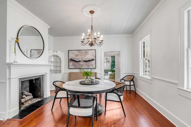 dining space with baseboards, wood-type flooring, a premium fireplace, an inviting chandelier, and crown molding