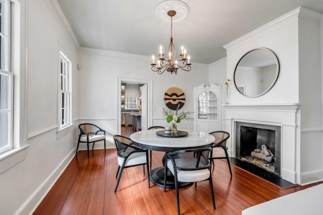 dining room featuring crown molding, a notable chandelier, a fireplace, baseboards, and hardwood / wood-style flooring