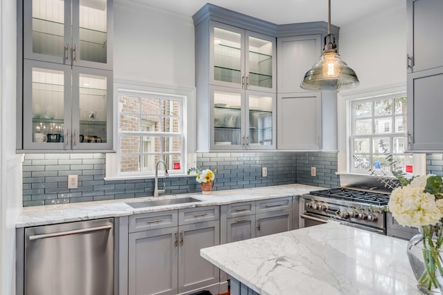 kitchen featuring gray cabinets, backsplash, appliances with stainless steel finishes, a sink, and light stone countertops