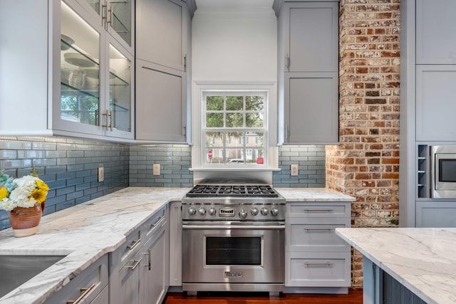 kitchen featuring light stone counters, crown molding, decorative backsplash, appliances with stainless steel finishes, and glass insert cabinets