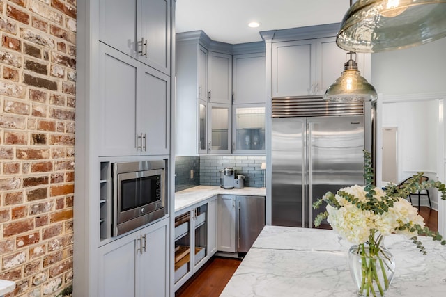 kitchen with light stone counters, dark wood-style flooring, backsplash, glass insert cabinets, and built in appliances