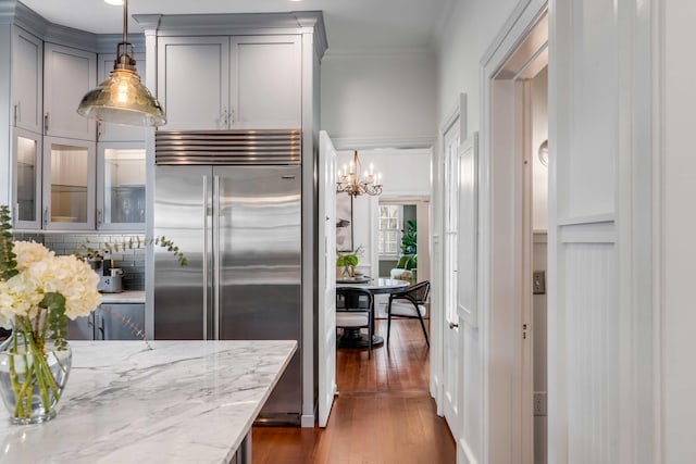 kitchen with crown molding, gray cabinets, dark wood-type flooring, light stone countertops, and built in refrigerator