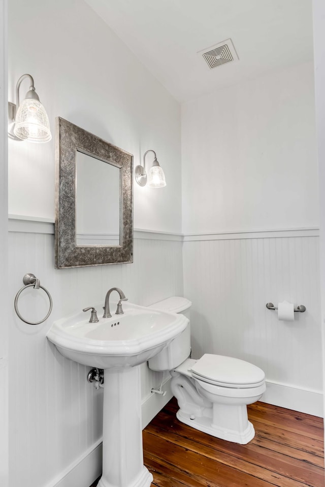 bathroom with toilet, visible vents, wood finished floors, and wainscoting