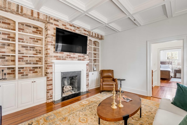 living area featuring hardwood / wood-style floors, a brick fireplace, coffered ceiling, beamed ceiling, and baseboards