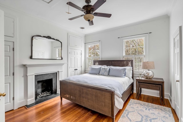 bedroom featuring baseboards, a fireplace, wood finished floors, and crown molding