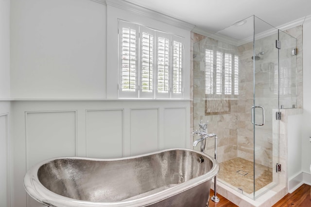 bathroom featuring a decorative wall, a wainscoted wall, ornamental molding, a soaking tub, and a stall shower