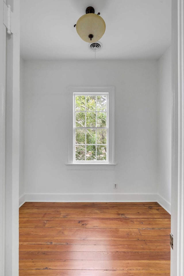 spare room featuring wood-type flooring, visible vents, and baseboards