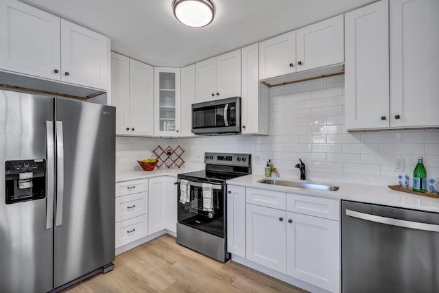 kitchen with sink, white cabinetry, appliances with stainless steel finishes, light hardwood / wood-style floors, and backsplash