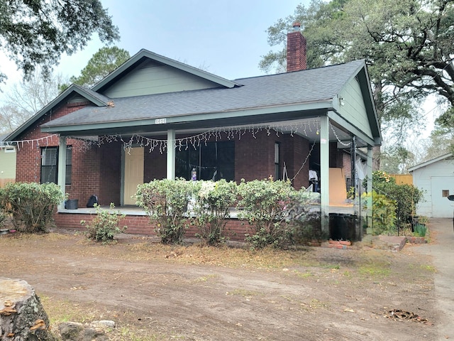 view of front of home featuring a shingled roof, a chimney, a porch, and brick siding