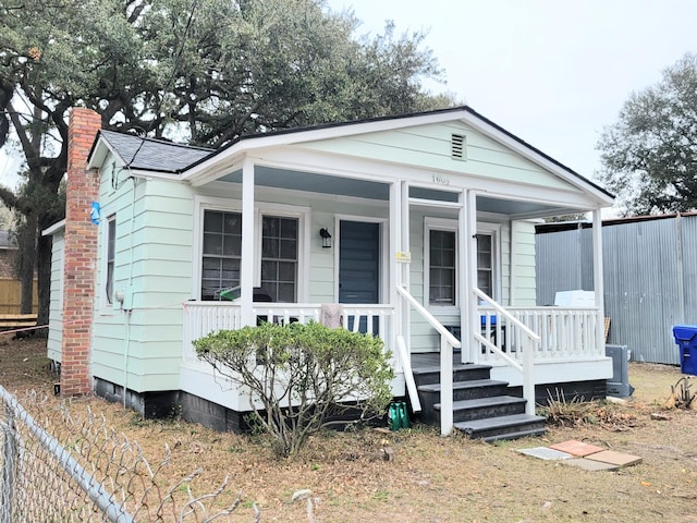 view of front of house with a shingled roof, covered porch, fence, and a chimney