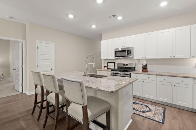 kitchen featuring visible vents, an island with sink, a sink, backsplash, and stainless steel appliances