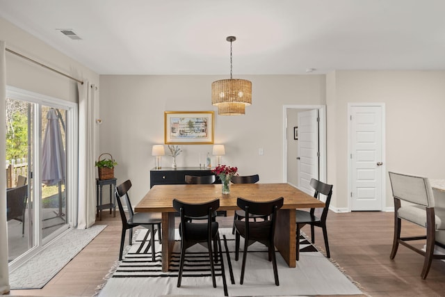 dining space featuring a notable chandelier, baseboards, visible vents, and wood finished floors