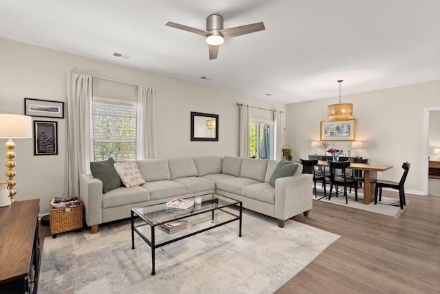 living room featuring light wood-type flooring, visible vents, baseboards, and a ceiling fan