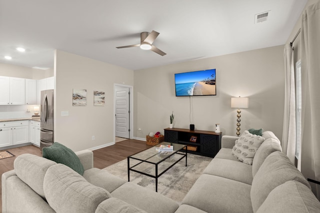 living room featuring light wood-type flooring, baseboards, visible vents, and a ceiling fan