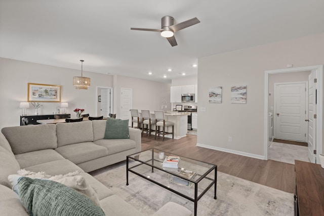 living room featuring recessed lighting, light wood-type flooring, baseboards, and ceiling fan with notable chandelier