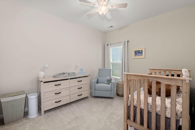 bedroom featuring light carpet, visible vents, a crib, and a ceiling fan