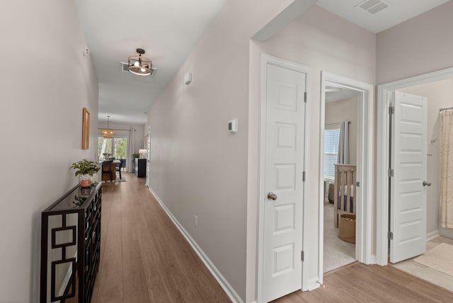 hallway featuring visible vents, baseboards, and wood finished floors