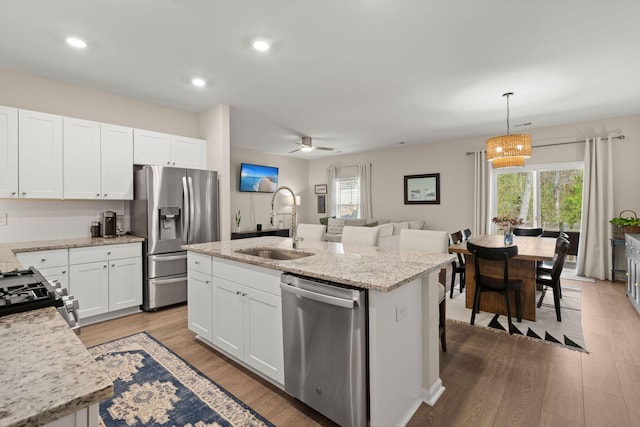 kitchen featuring wood finished floors, a center island with sink, a sink, white cabinets, and appliances with stainless steel finishes