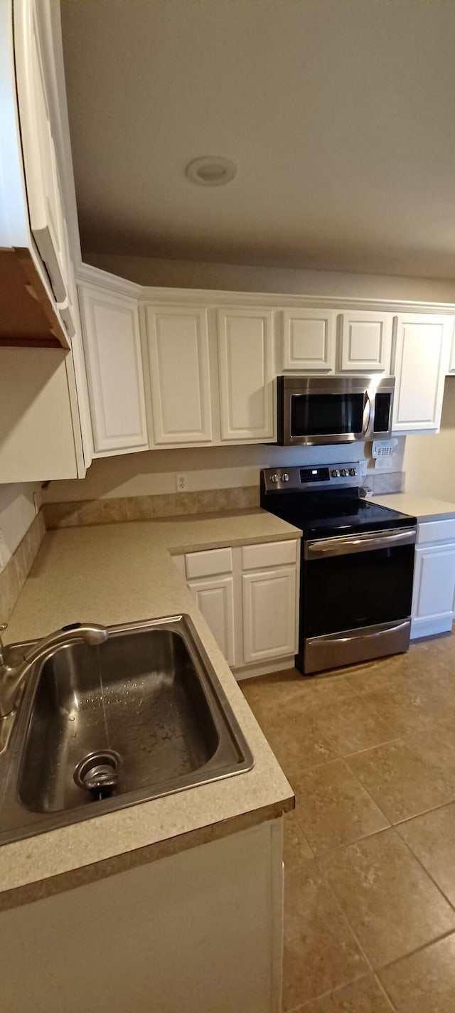 kitchen with light tile patterned flooring, appliances with stainless steel finishes, white cabinetry, and sink