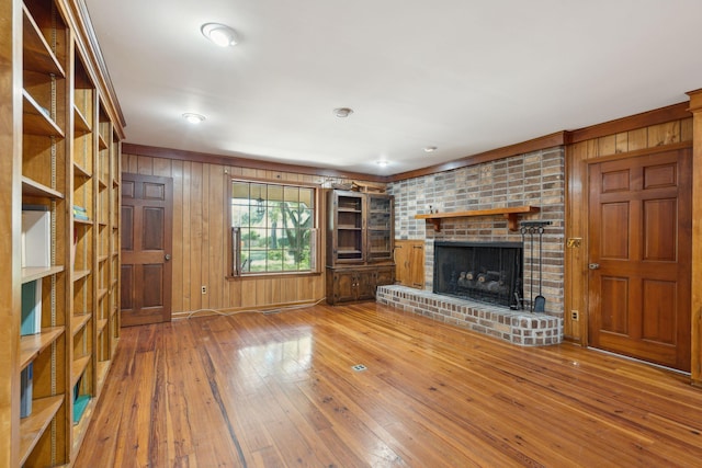 unfurnished living room featuring a brick fireplace, wood walls, and hardwood / wood-style flooring