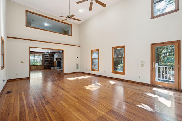 unfurnished living room featuring wood-type flooring, high vaulted ceiling, ceiling fan, and a brick fireplace