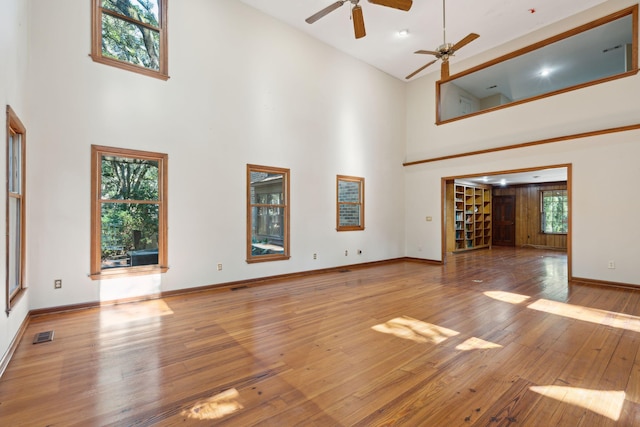 unfurnished living room with ceiling fan, light wood-type flooring, and a towering ceiling