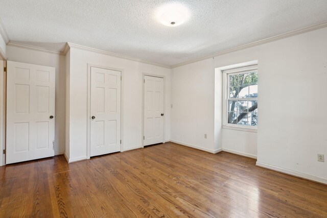 unfurnished bedroom with wood-type flooring, a textured ceiling, two closets, and ornamental molding