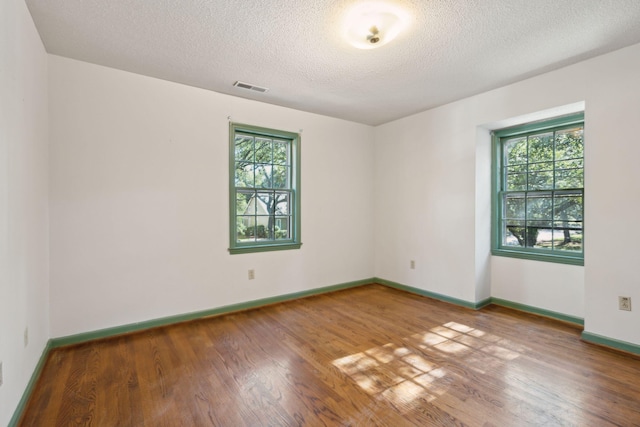 empty room with hardwood / wood-style flooring, a textured ceiling, and a wealth of natural light