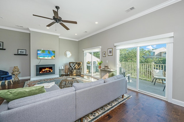 living room featuring visible vents, baseboards, ornamental molding, dark wood finished floors, and a lit fireplace
