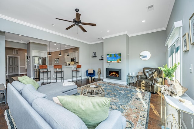 living area featuring baseboards, dark wood finished floors, crown molding, visible vents, and ceiling fan