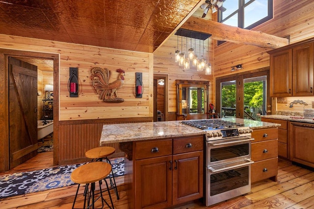 kitchen featuring light stone countertops, wood walls, pendant lighting, range with two ovens, and a kitchen bar