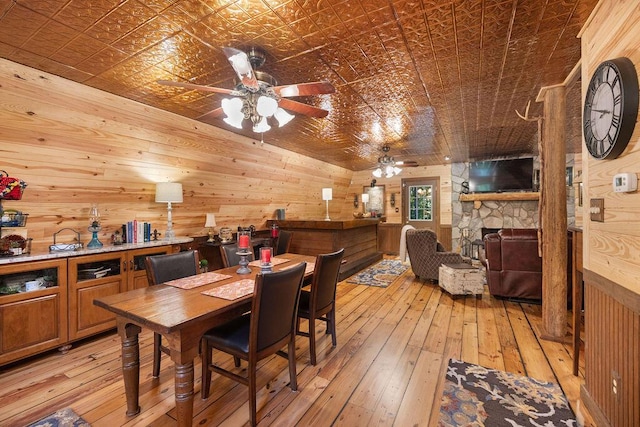 dining area with ceiling fan, a fireplace, light hardwood / wood-style floors, and wood walls