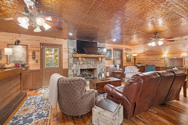 living room featuring ceiling fan, wood walls, a stone fireplace, and wood-type flooring