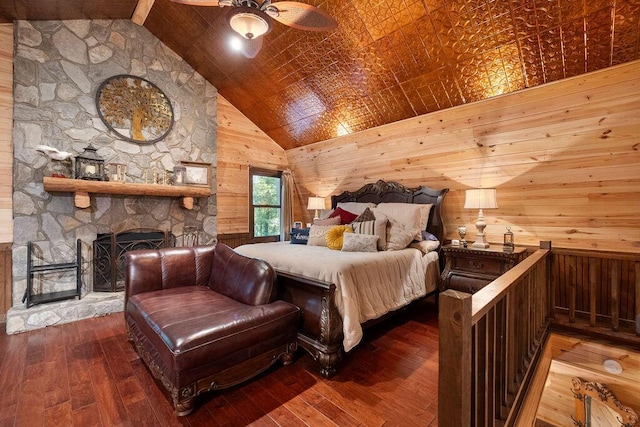 bedroom featuring hardwood / wood-style flooring, wood walls, a stone fireplace, and high vaulted ceiling